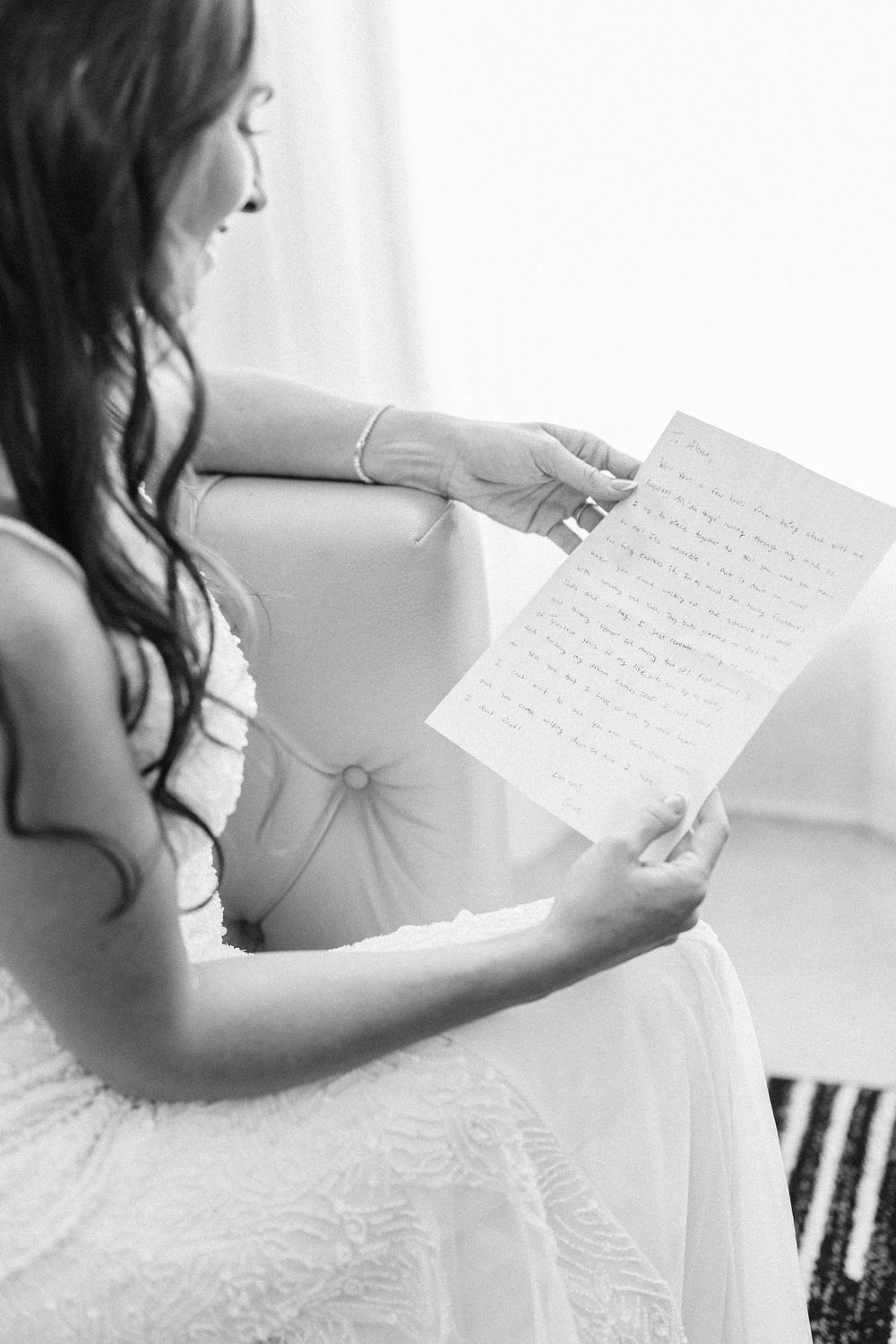 A person wearing a white bridal gown reads a handwritten letter in black and white photography.