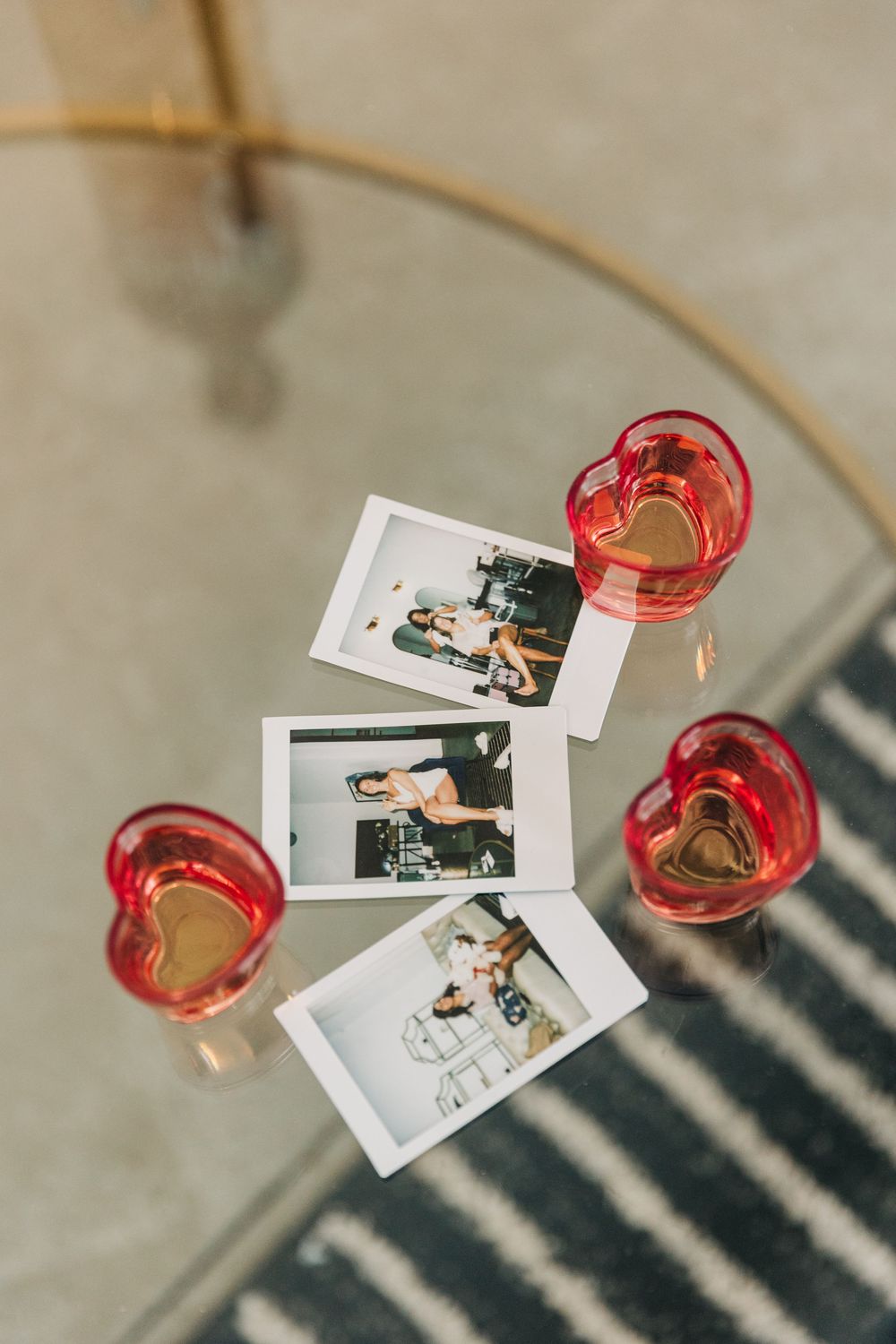 Polaroid photos scattered on table next to red heart-shaped champagne glasses casting dramatic window shadows.