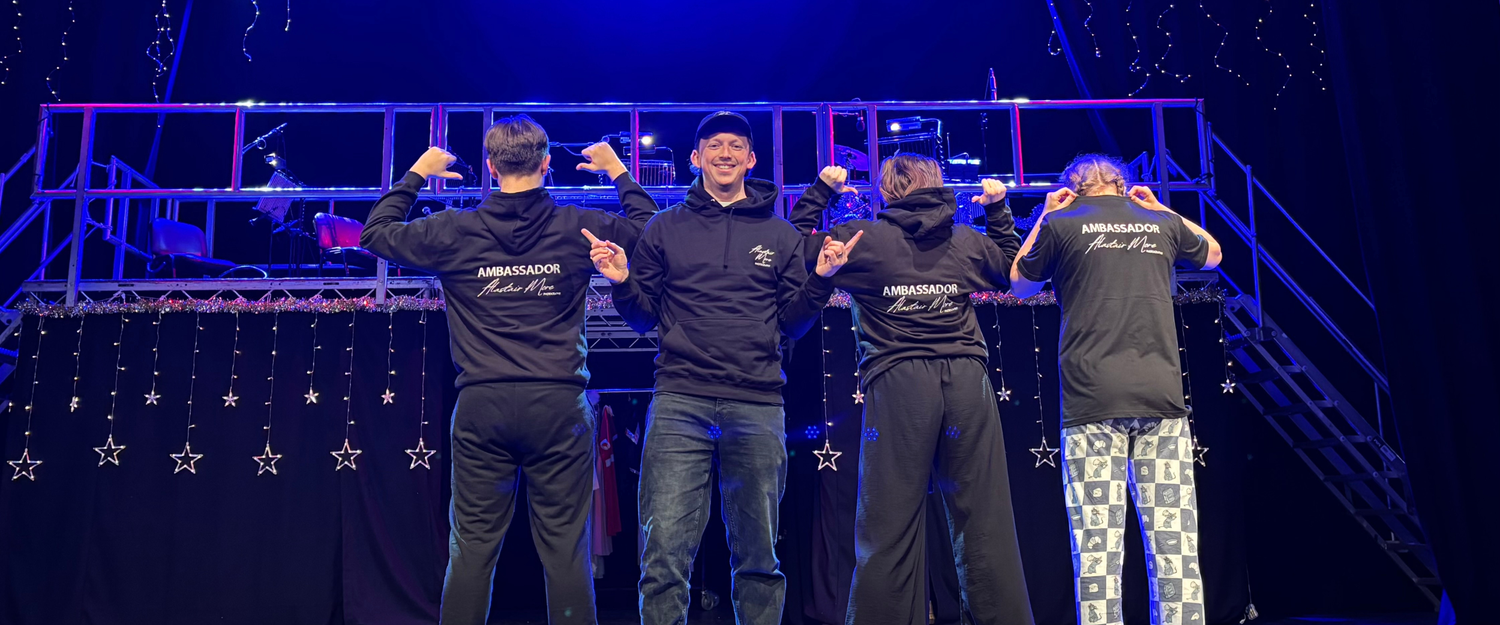 Three performers in black outfits stand in dramatic purple stage lighting creating a theatrical silhouette effect.
