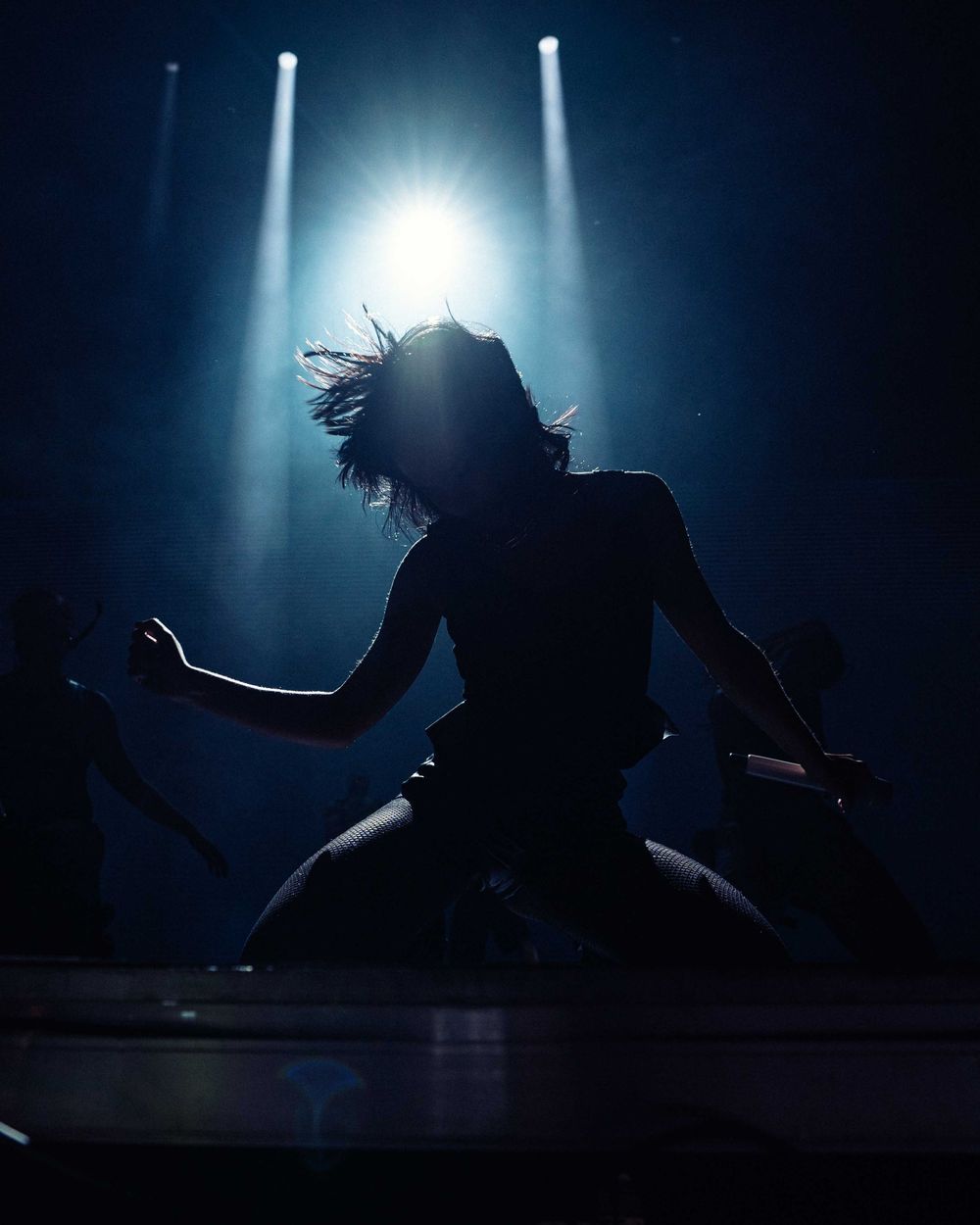 Dramatic silhouettes of dancers performing under bright spotlights on dark stage.