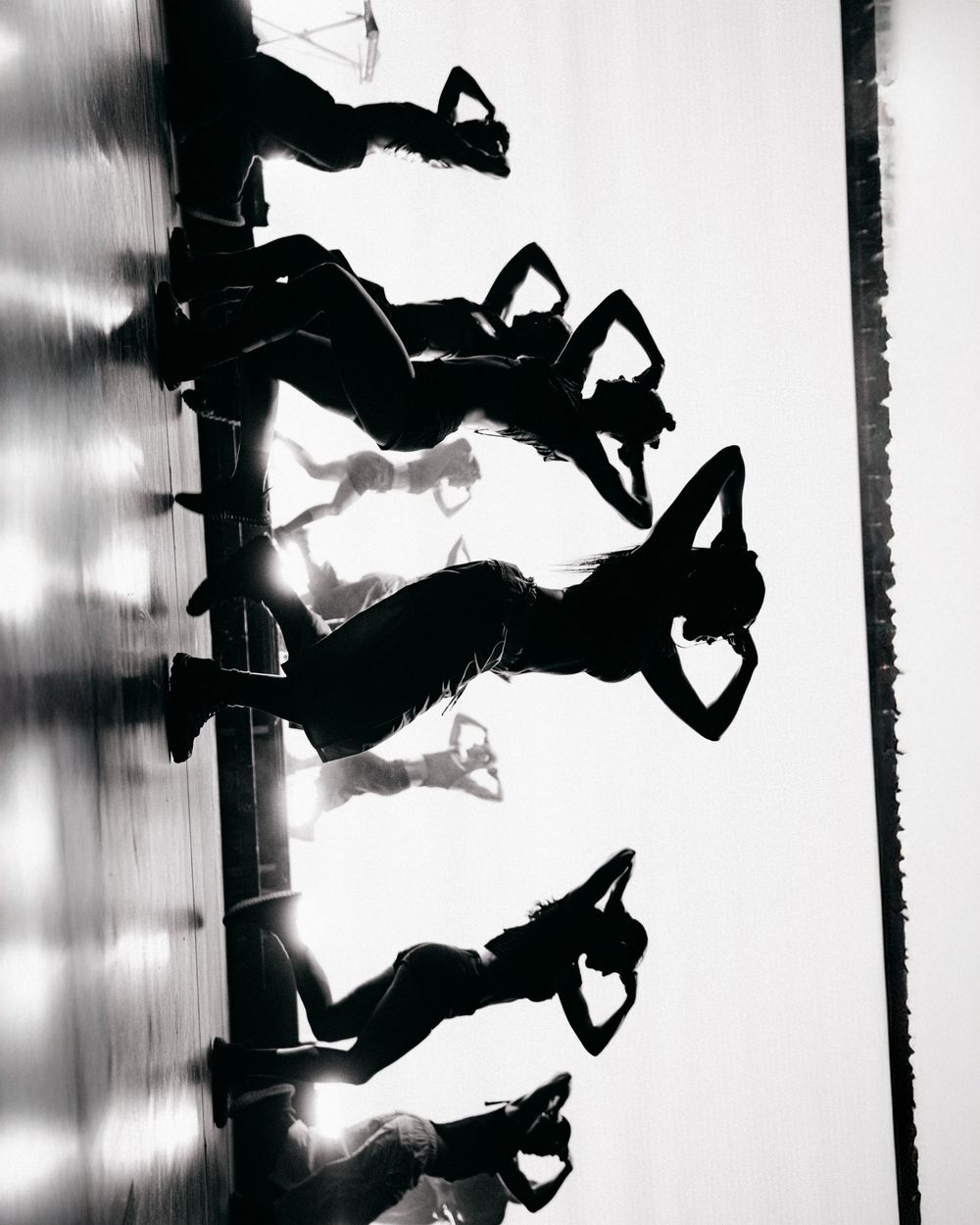 Black and white silhouette of five people jumping in synchronized formation casting dramatic shadows.