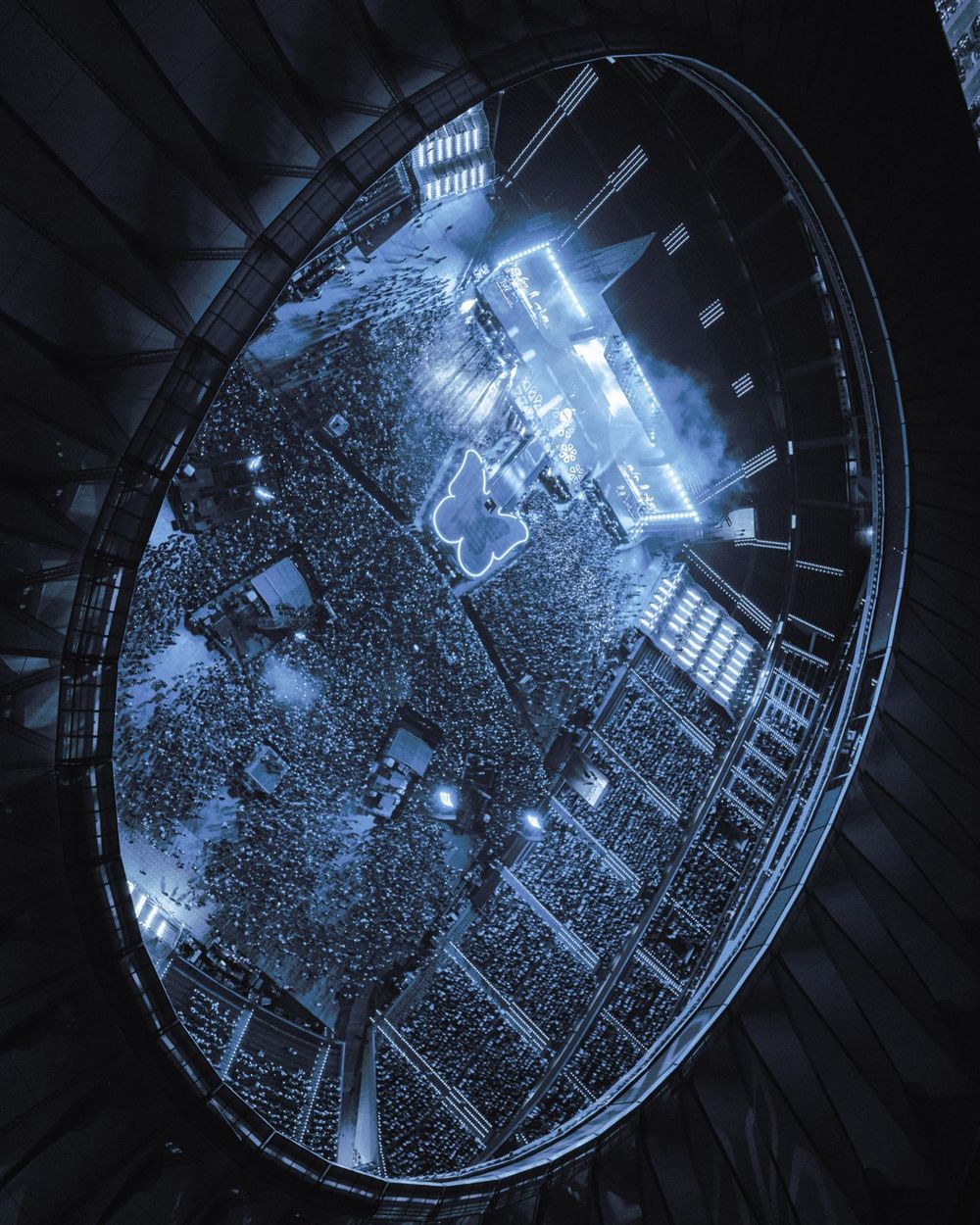 Upward view through a circular skylight showing a crowd of people gathered beneath blue-tinted architectural details.