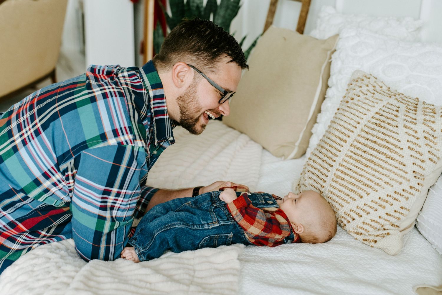 Parent and baby share tender moments while playing on a cozy bed with plush pillows and blankets.