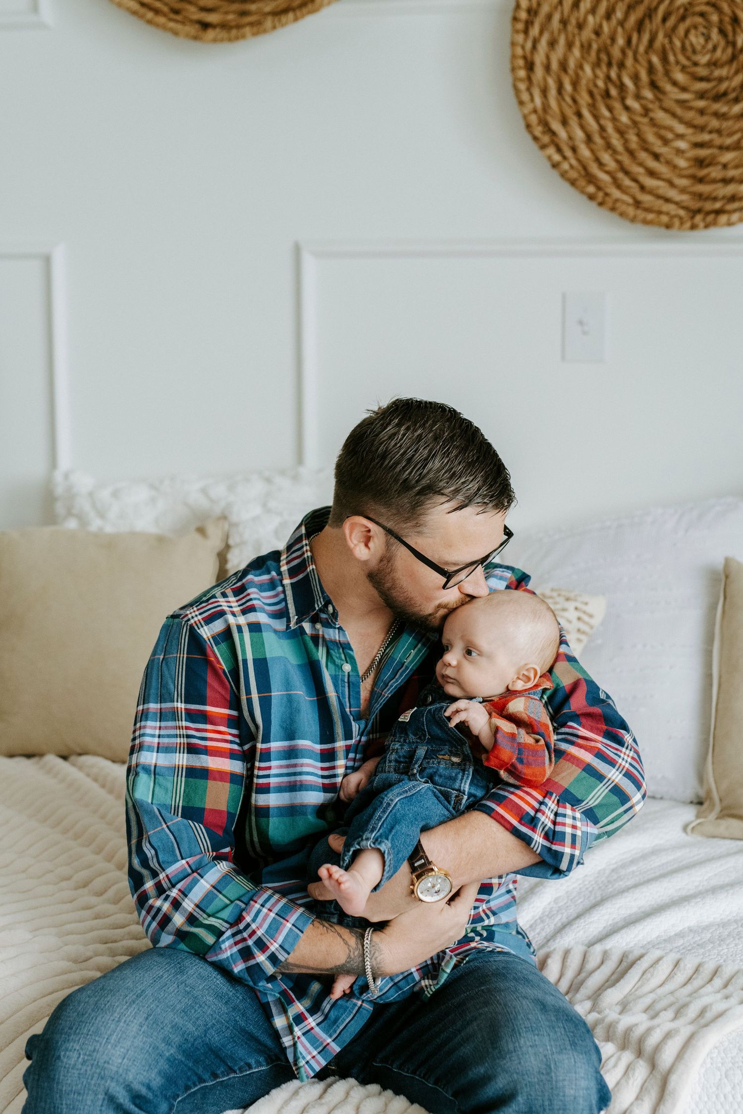 A plaid-shirted figure sits on a bed with a small child while decorative woven baskets hang on the wall behind them.