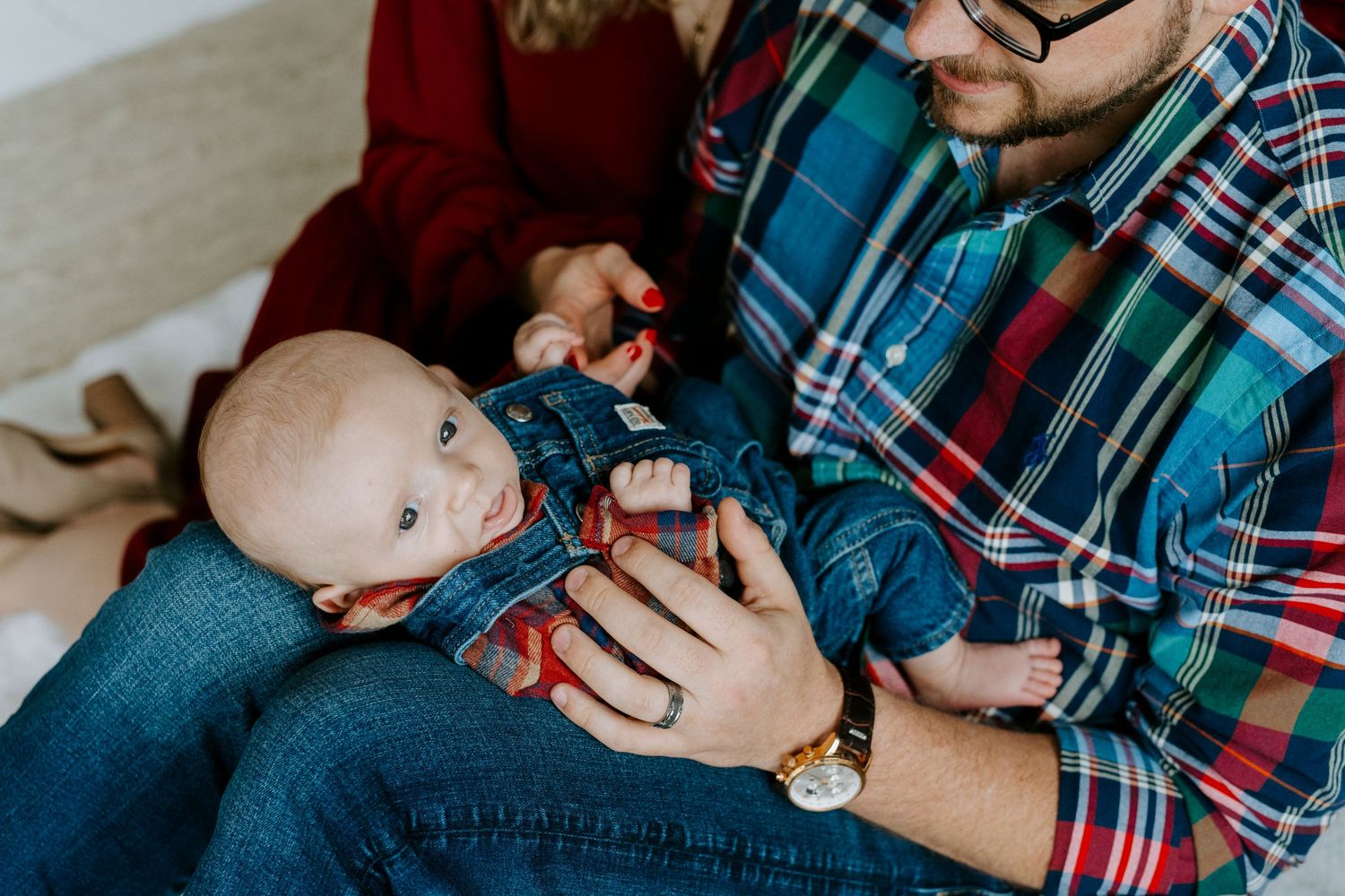 A person in a plaid shirt holds and feeds a baby with a bottle while sitting in a chair.