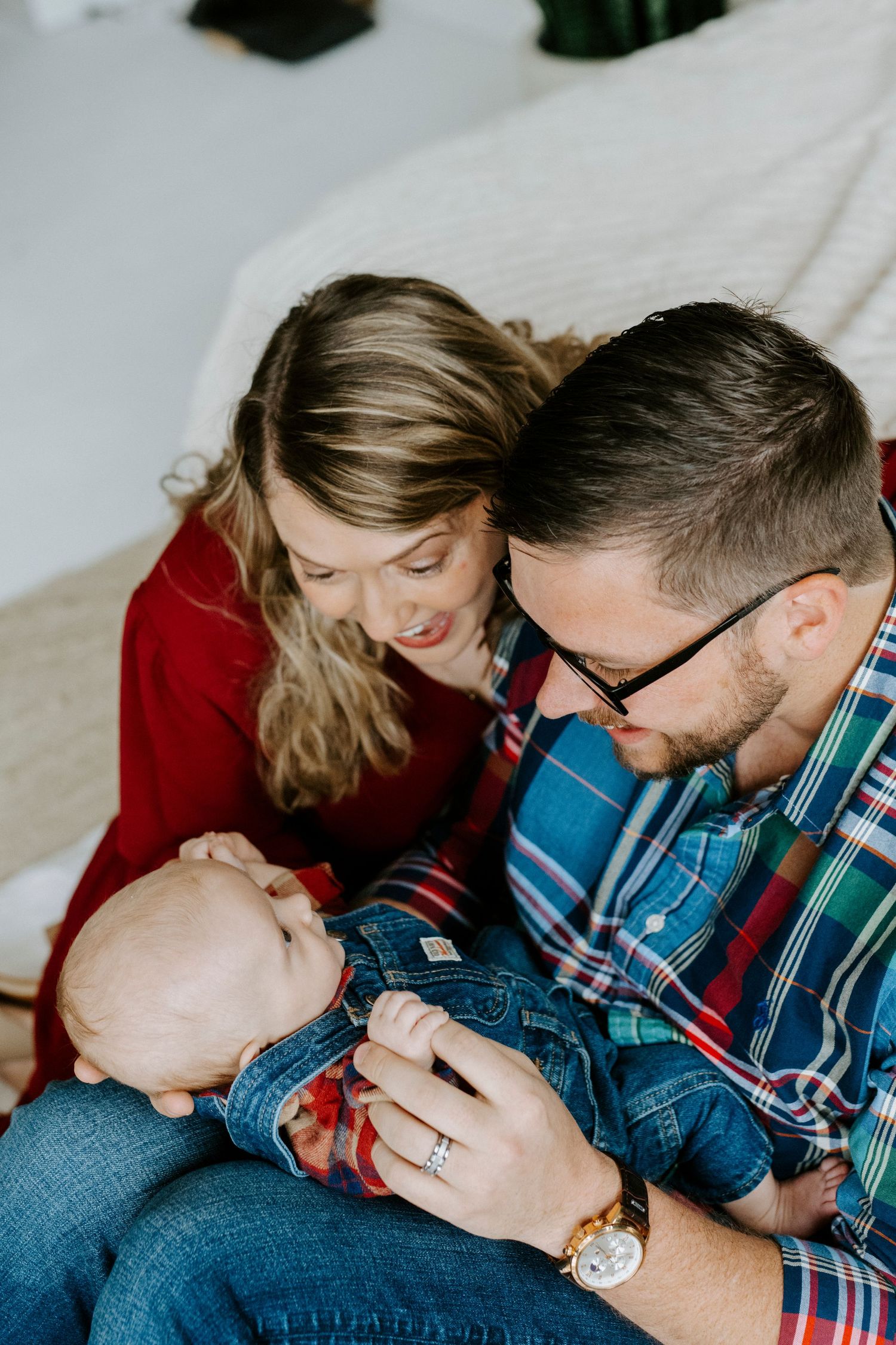 A tender family moment captured in a series of candid photos showing parents cuddling with their baby on a light background.