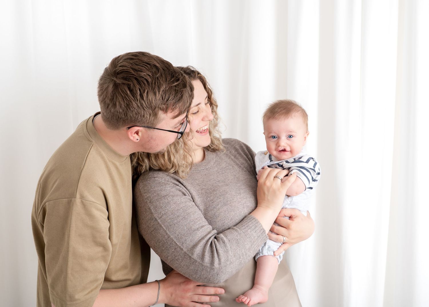 Intimate family portrait showing tender moment with baby against white backdrop.