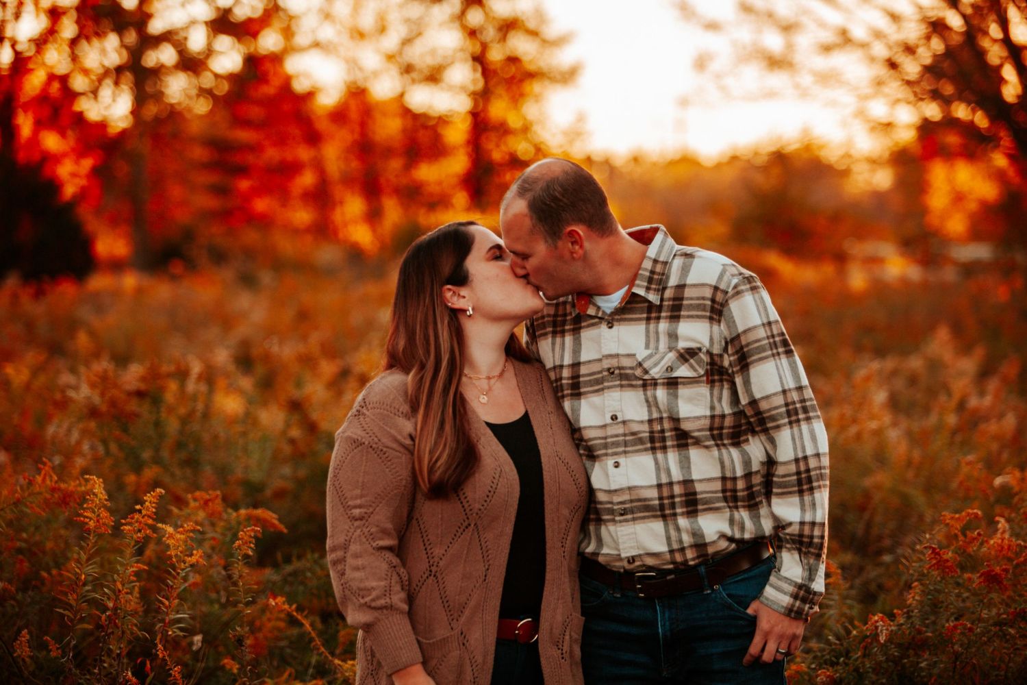 A couple shares an intimate moment in a rustic autumn setting with golden sunlight filtering through.