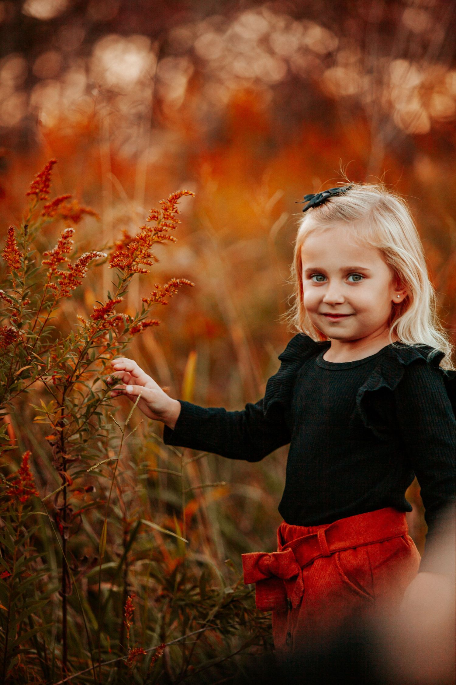 A small child in black and red explores autumn wildflowers during golden hour.