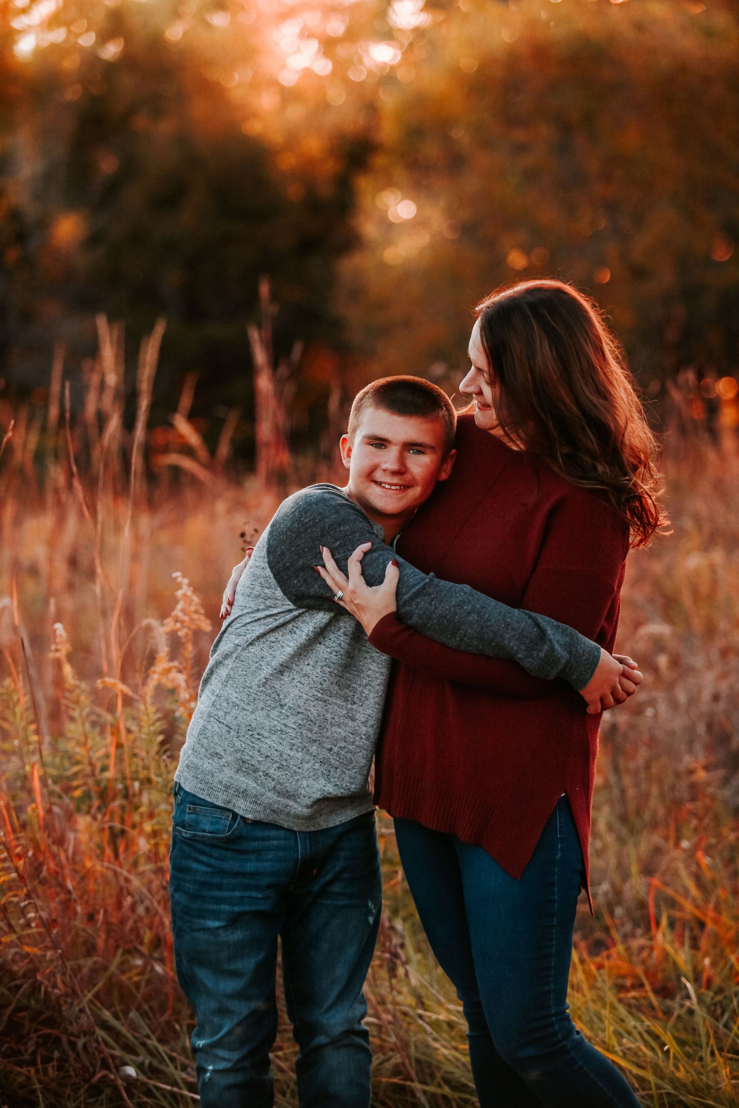 Two people share a playful hug among tall grasses during sunset.