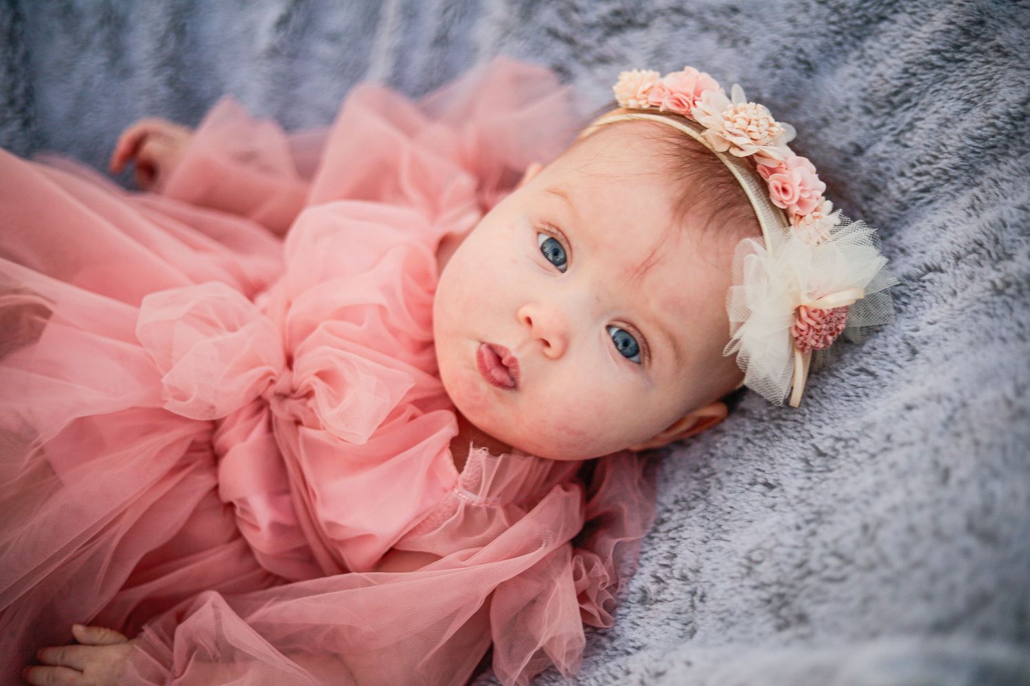 A baby in pink tulle dress lies on soft gray blanket during a portrait session.