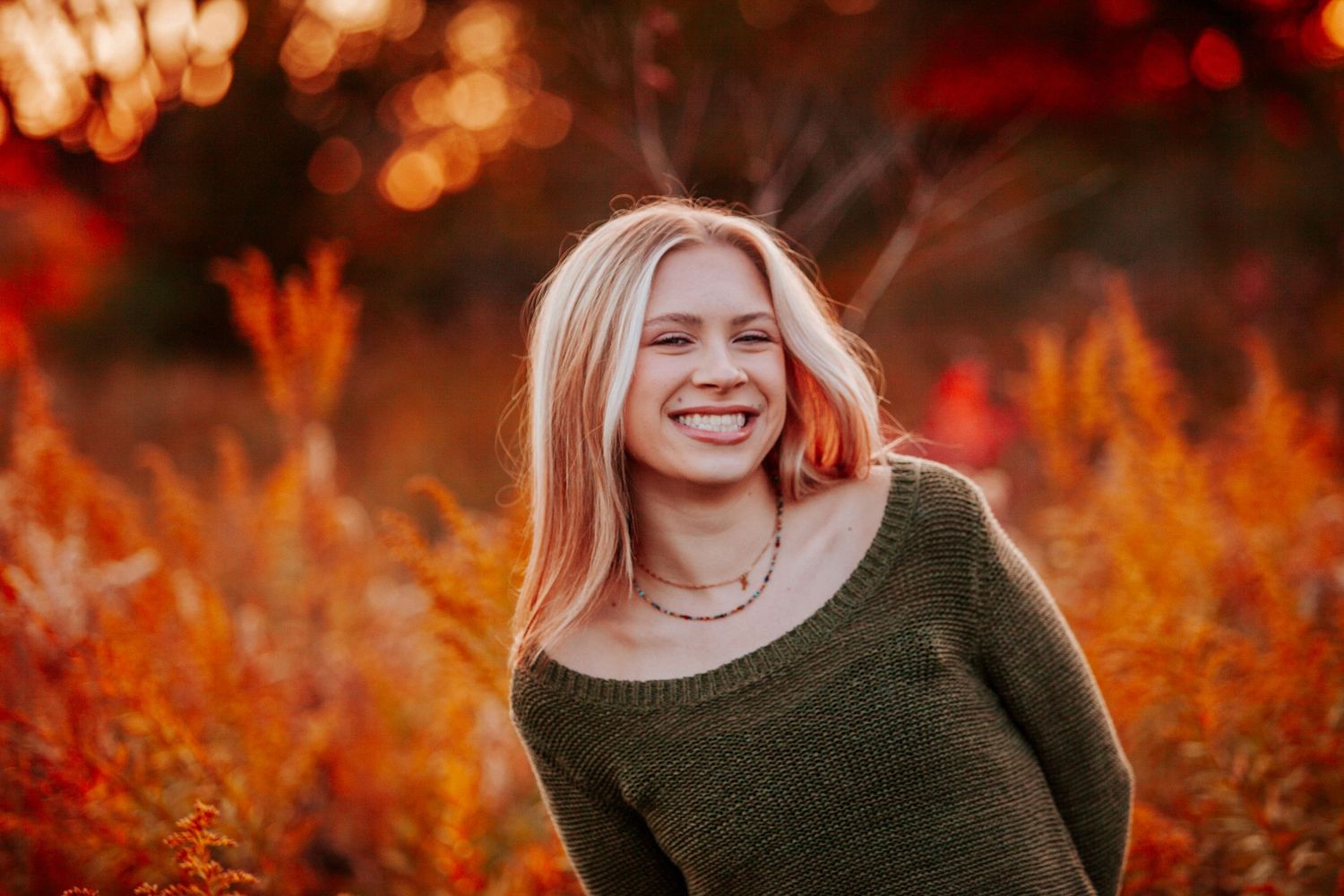 Portrait against vibrant orange autumn foliage with bokeh lighting effects.