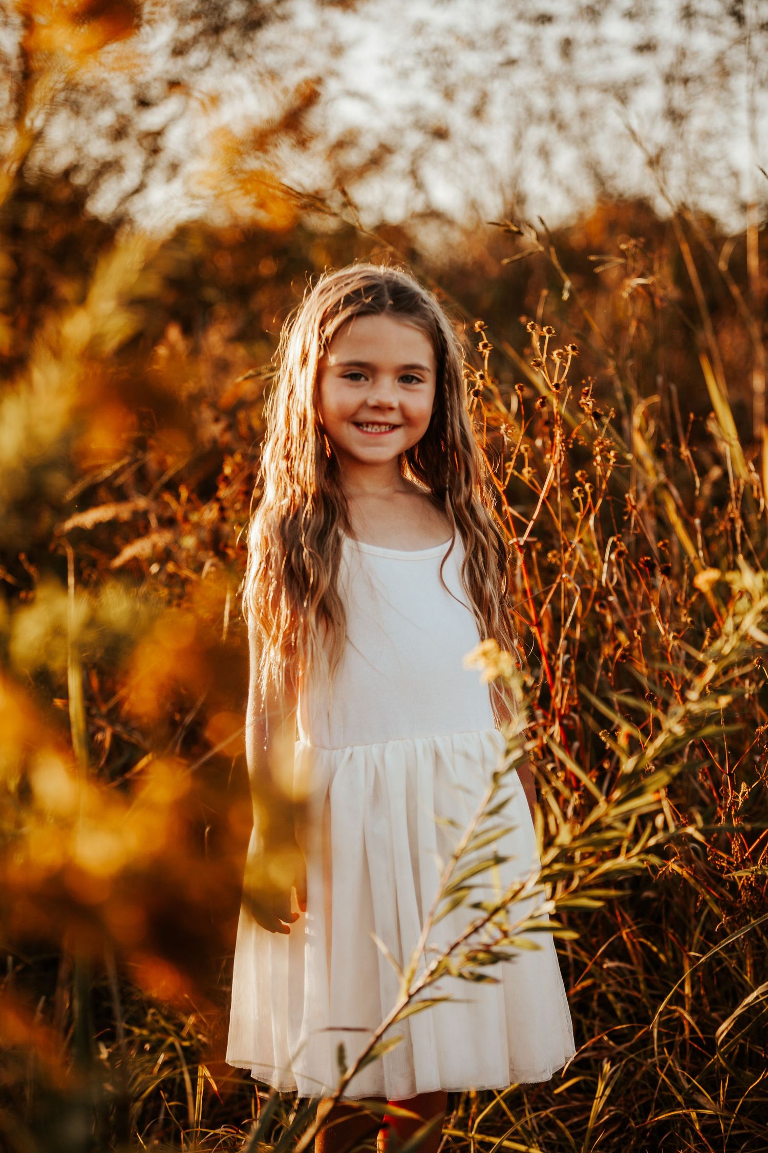 White dress contrasts beautifully against warm autumn grass at golden hour.