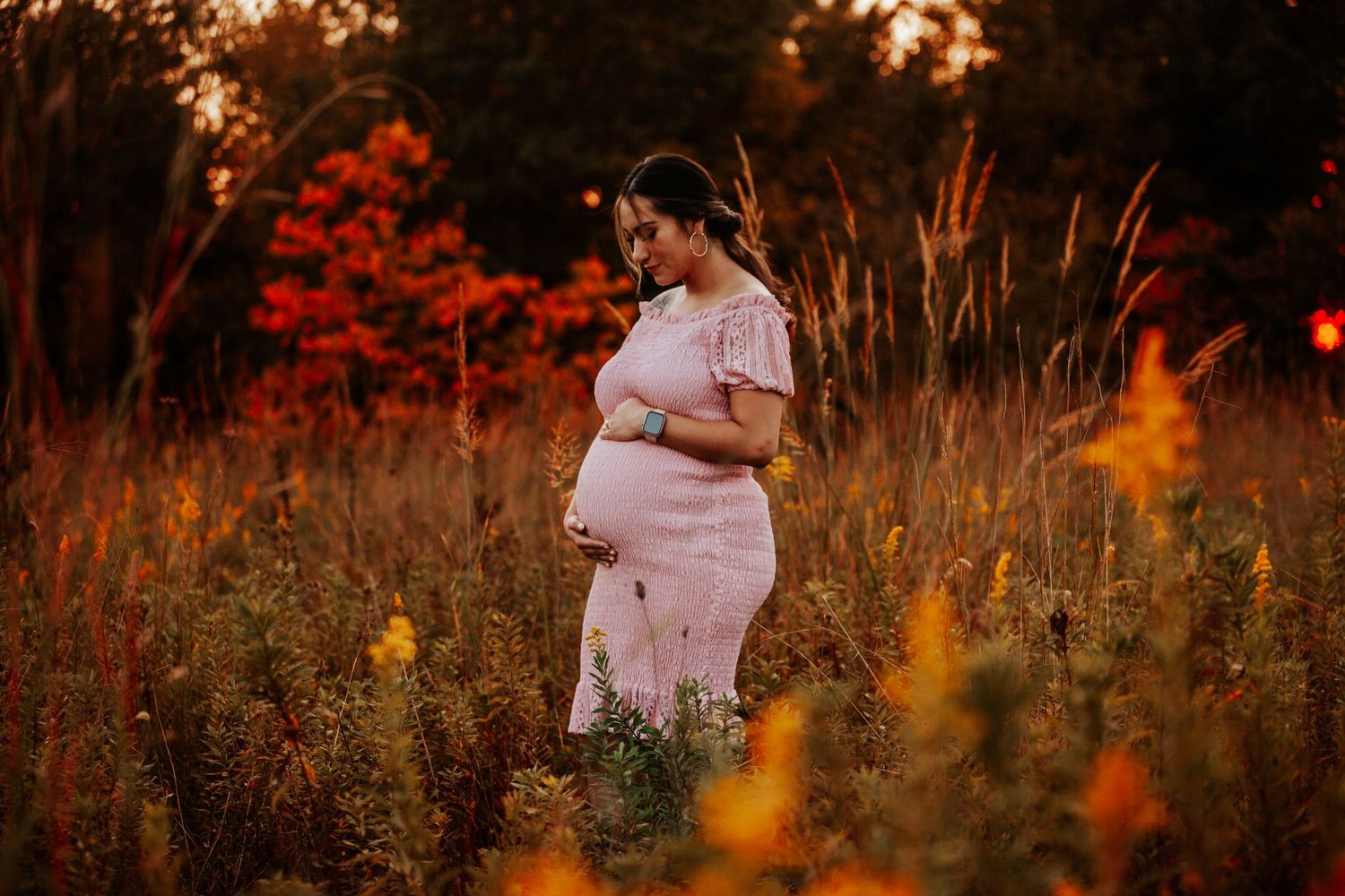 A person in a pink dress stands among wildflowers during a warm autumn sunset.