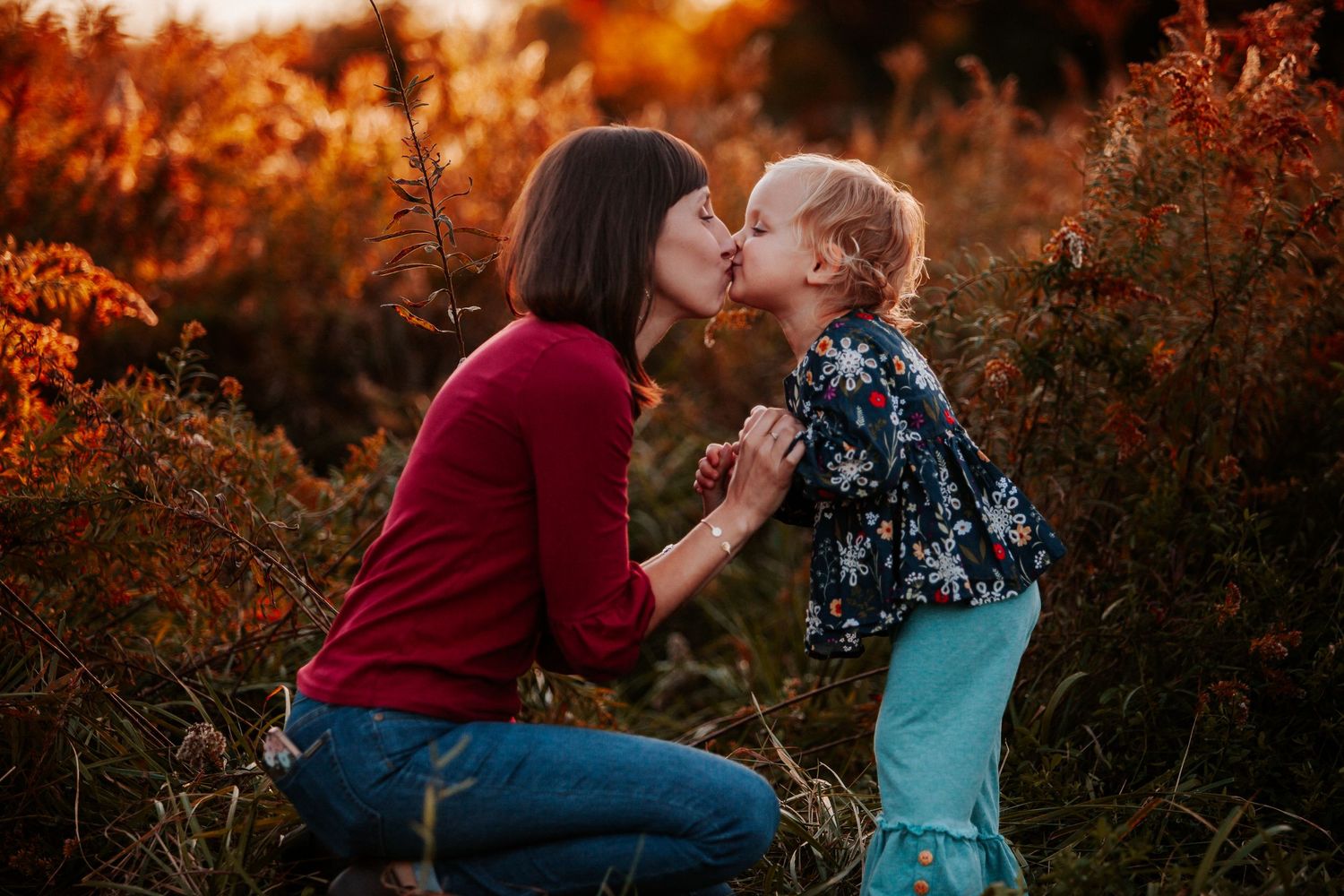 A couple shares a romantic moment in a field during golden hour with warm autumn colors in the background.