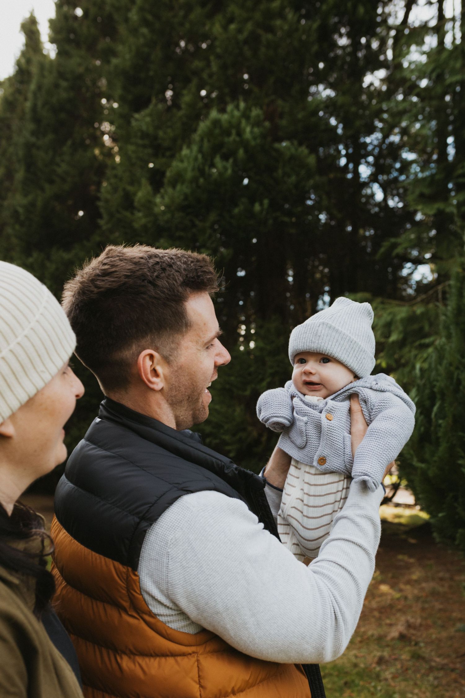 Winter outdoor portrait with bundled figures and small baby against evergreen trees.