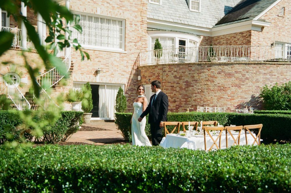 Newlyweds walking through a lush garden while holding hands at an elegant brick estate venue.