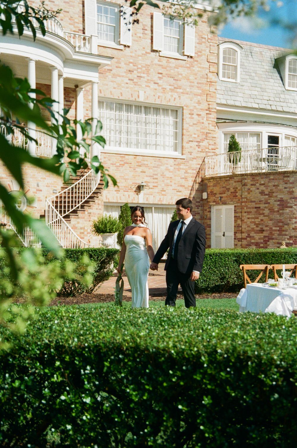 Scenic garden view of an elegant brick mansion with pristine landscaping and ornate white columns.