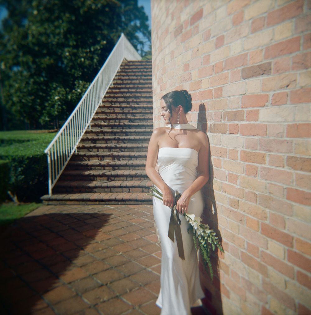 A couple in formal wedding attire embraces by a brick wall while casting dramatic shadows.
