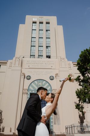 Elopement at the San Diego County Clerks office, couple kissing in front of building with bouquet raised