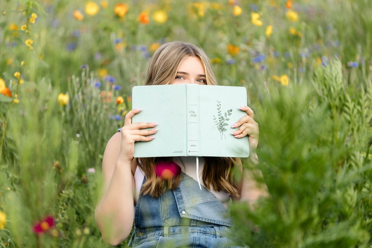 A person holds up a wooden sign in a meadow filled with colorful wildflowers during a sunny day.