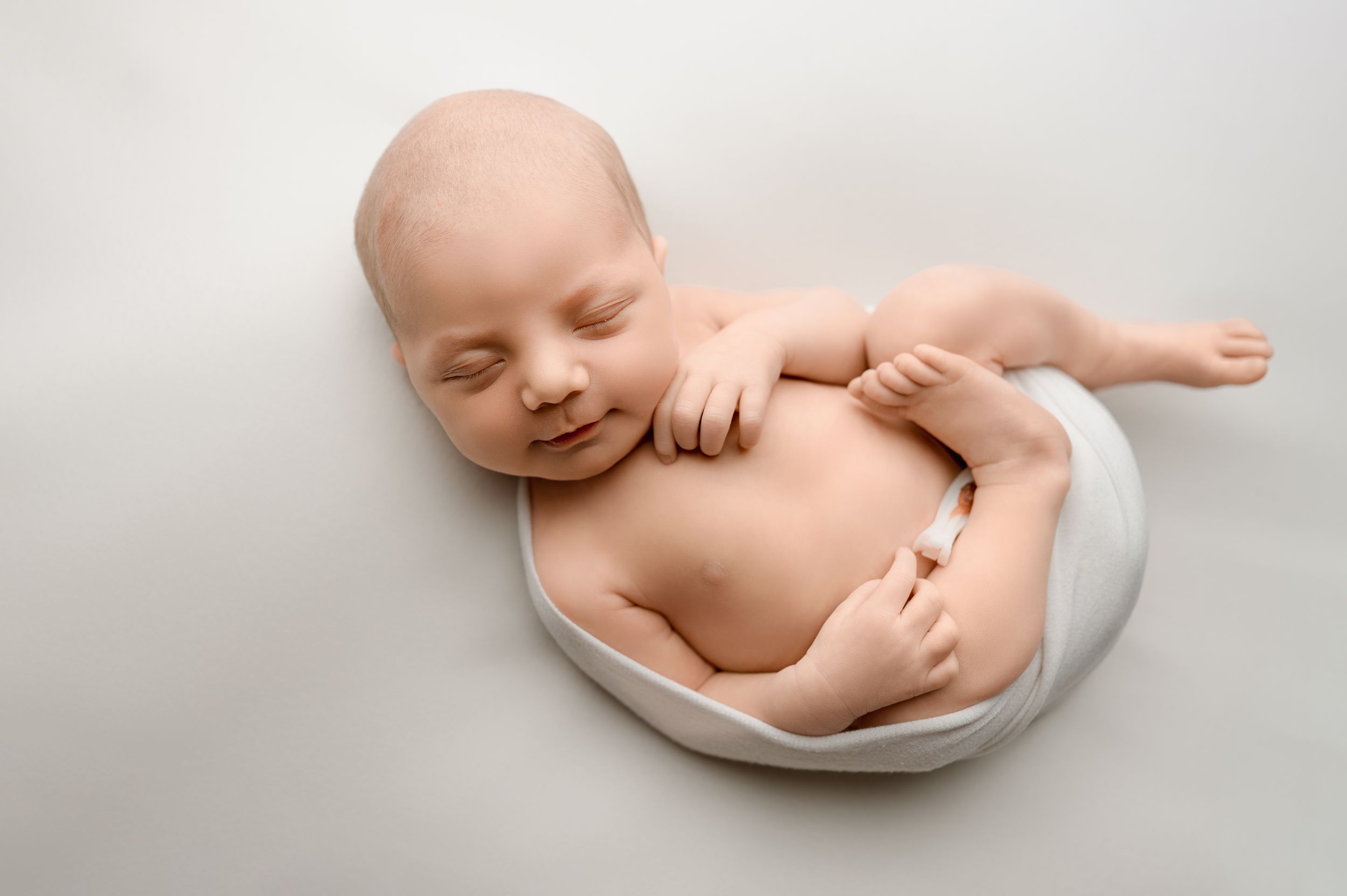 Peaceful newborn baby sleeping on a soft white fabric in a studio photography setting.