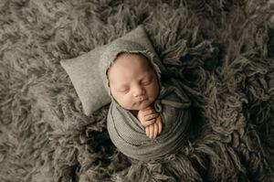 A peaceful sleeping newborn baby wrapped in gray fabric lies on soft fur blankets during a professional photo session.