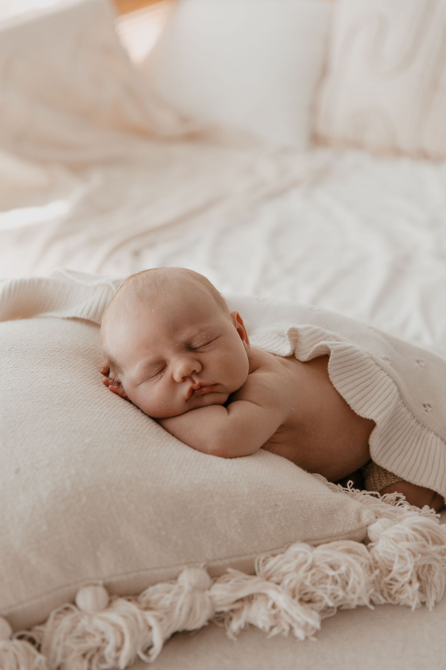 Sleeping newborn baby on textured white bedding in soft natural light.
