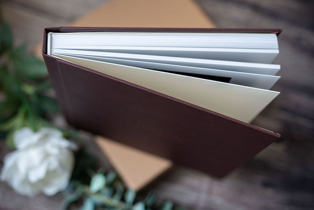 Close-up view of an open leather-bound book with crisp white pages against a blurred floral background.