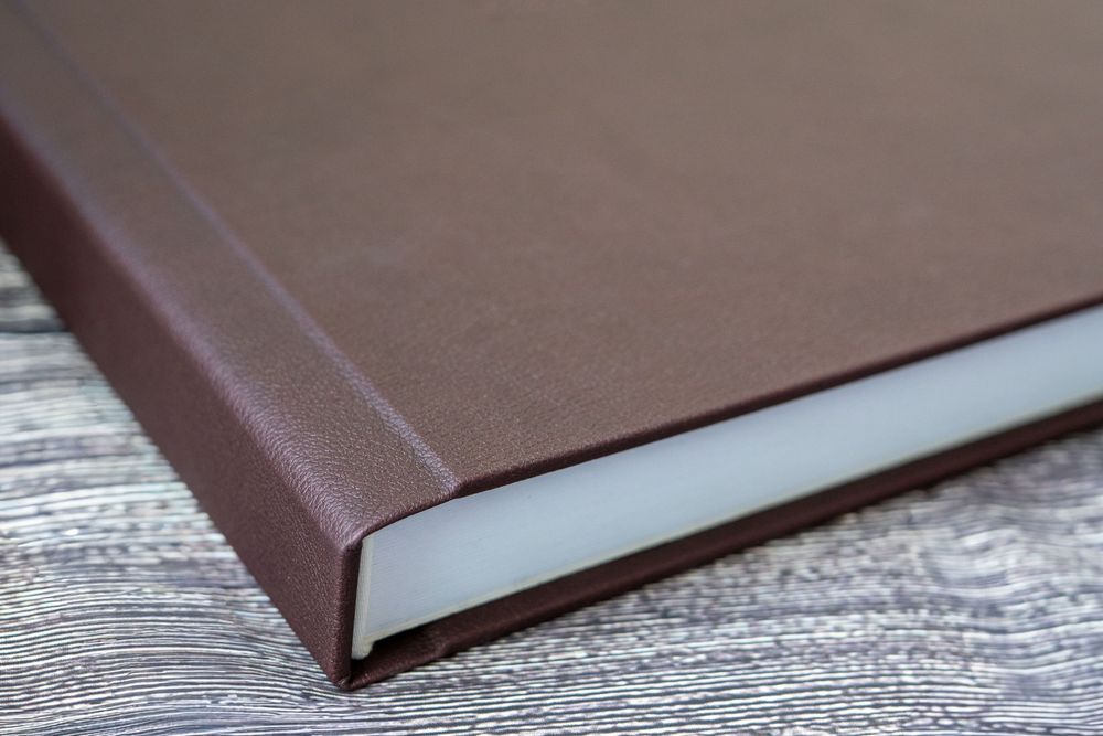 Brown hardcover vertical spine of a book shown in a progressive sequence of close-up shots against wooden background.