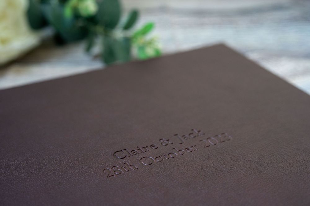 Close-up view of dark brown leather with embossed text on a blurred surface near green foliage.