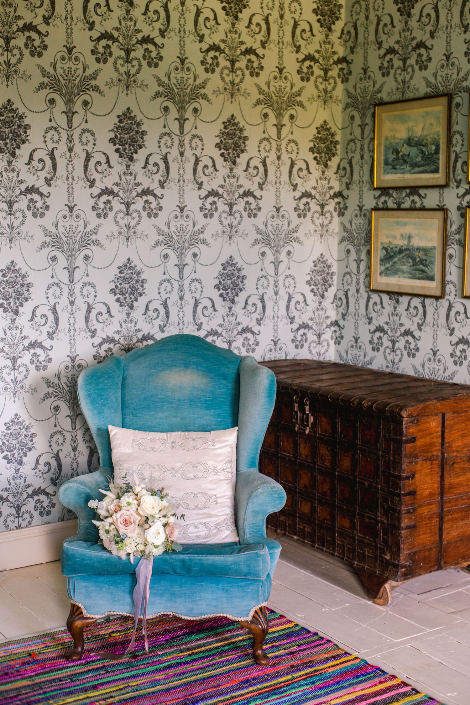 Vintage room with damask wallpaper, turquoise armchair and antique wooden chest.