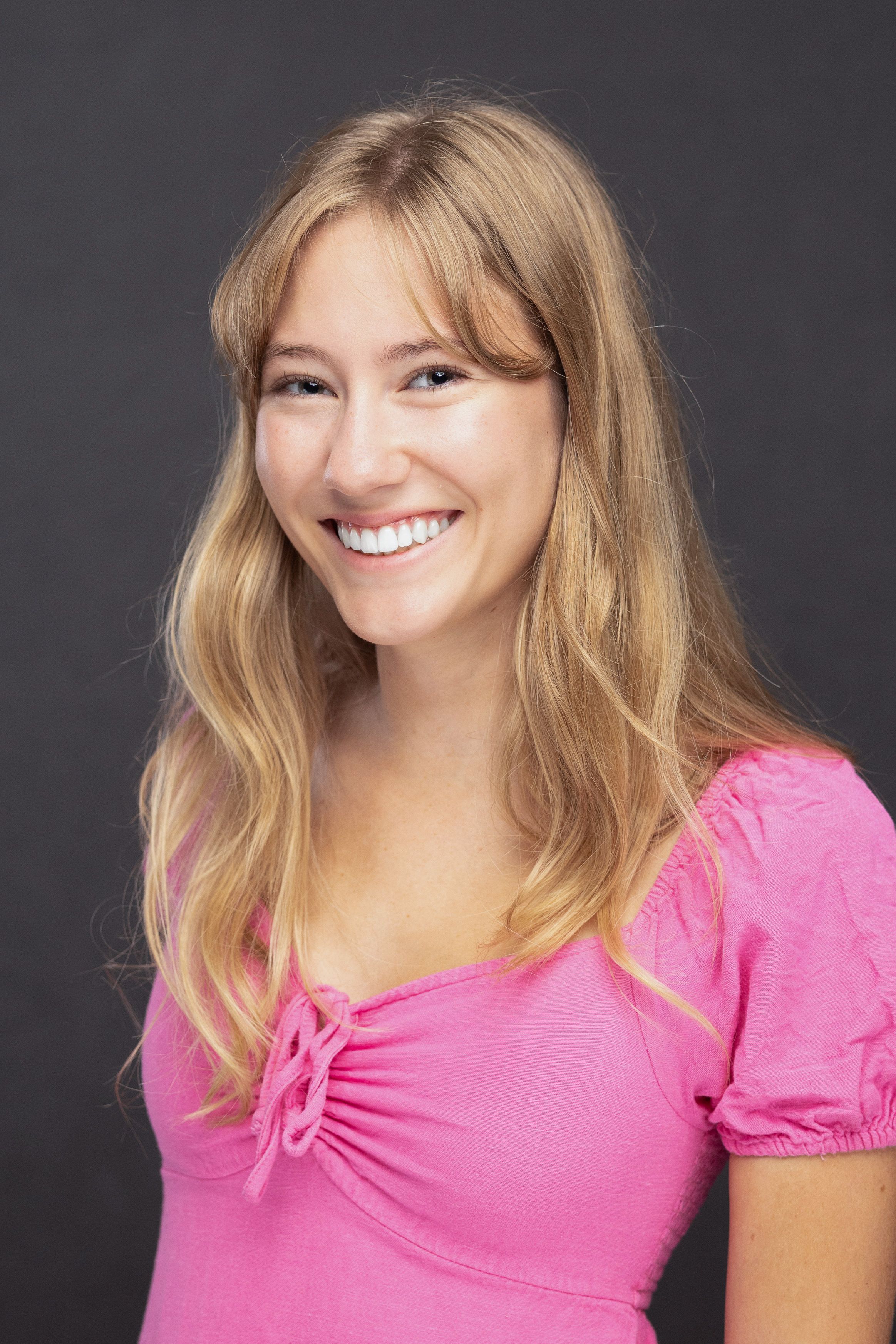 Headshot of a smiling young woman in a pink top against a dark background