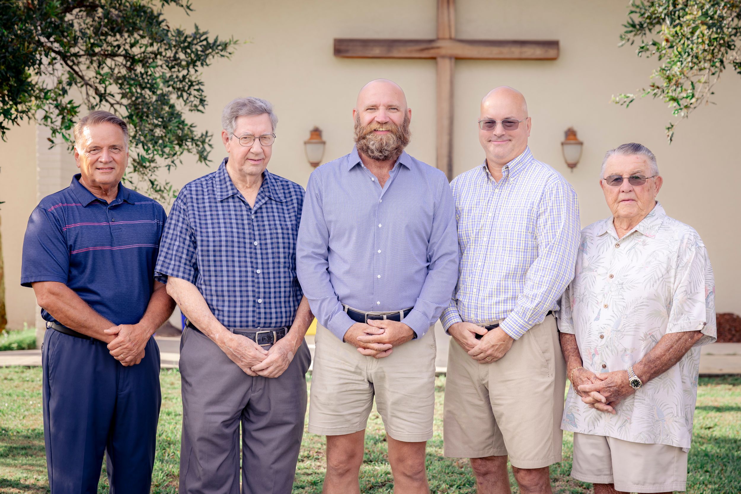 Group portrait of five men standing in front of a church wall with a cross