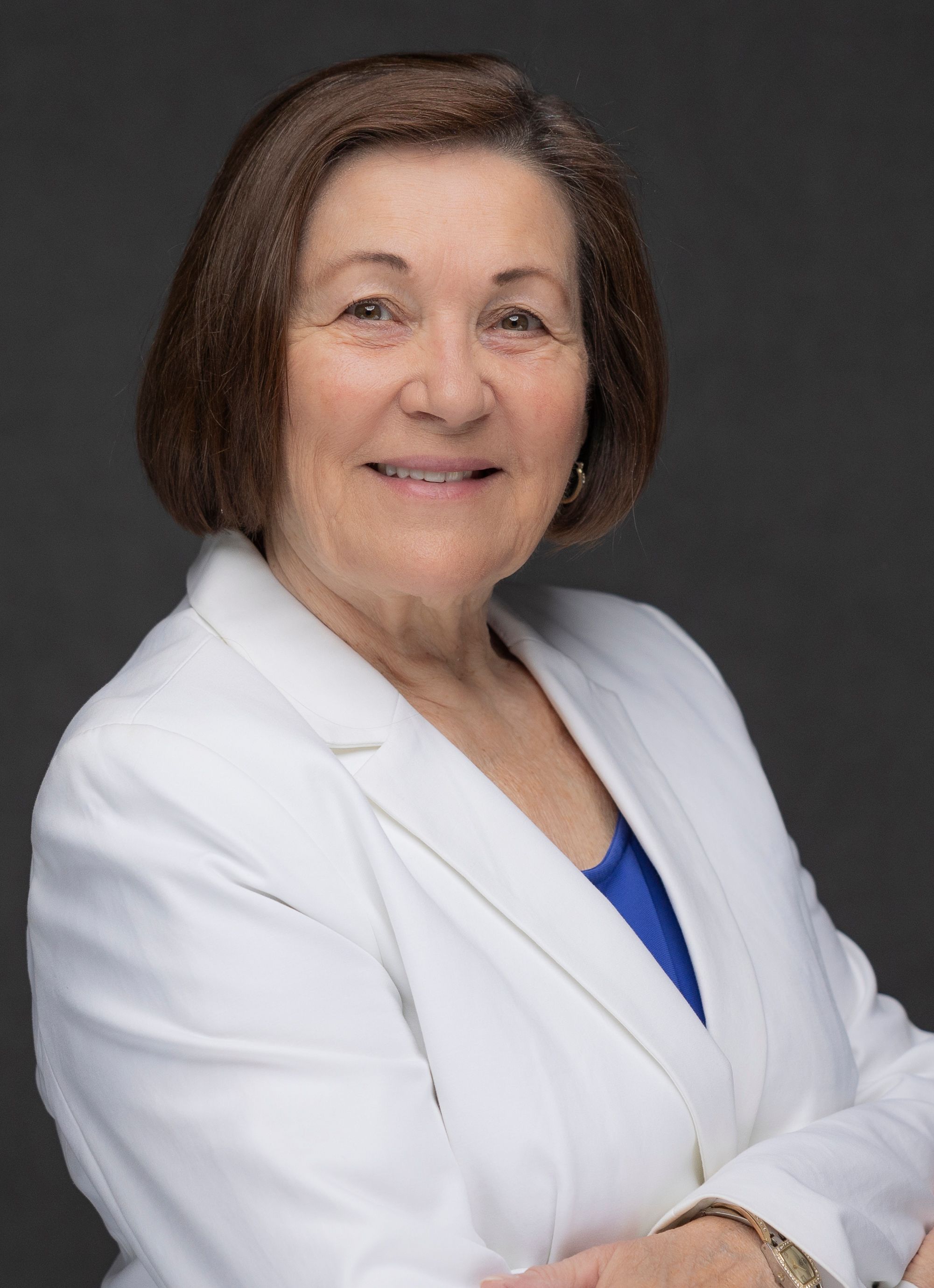 Professional headshot of a woman in a white blazer against a gray background