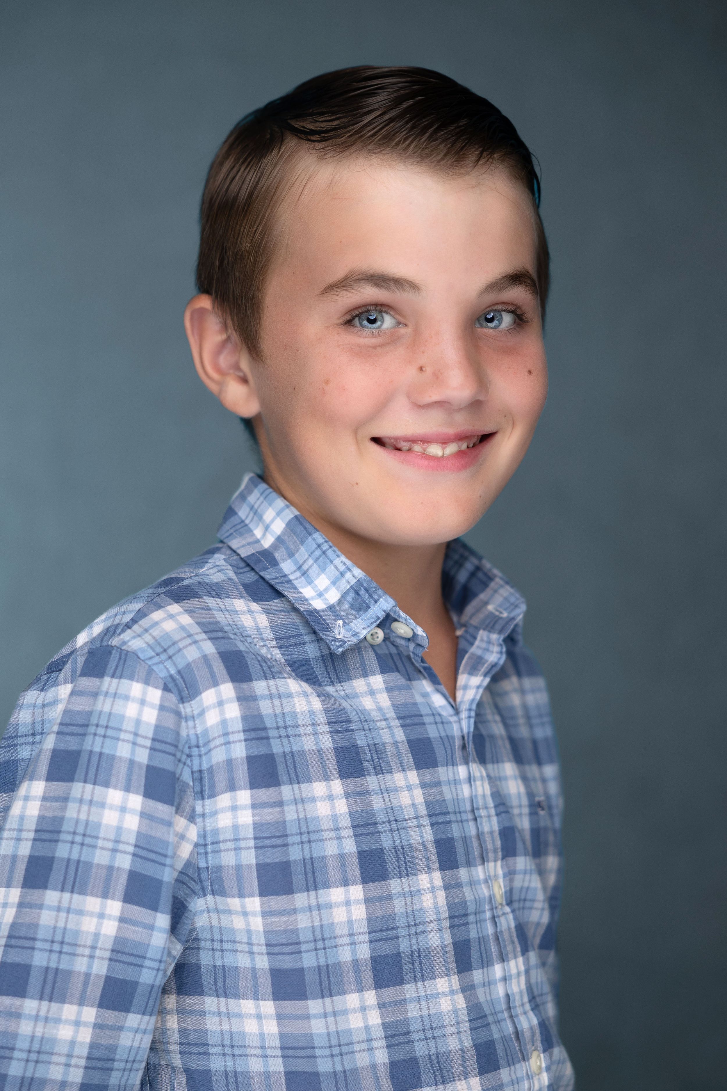 Portrait of a smiling boy in a plaid shirt against a dark background