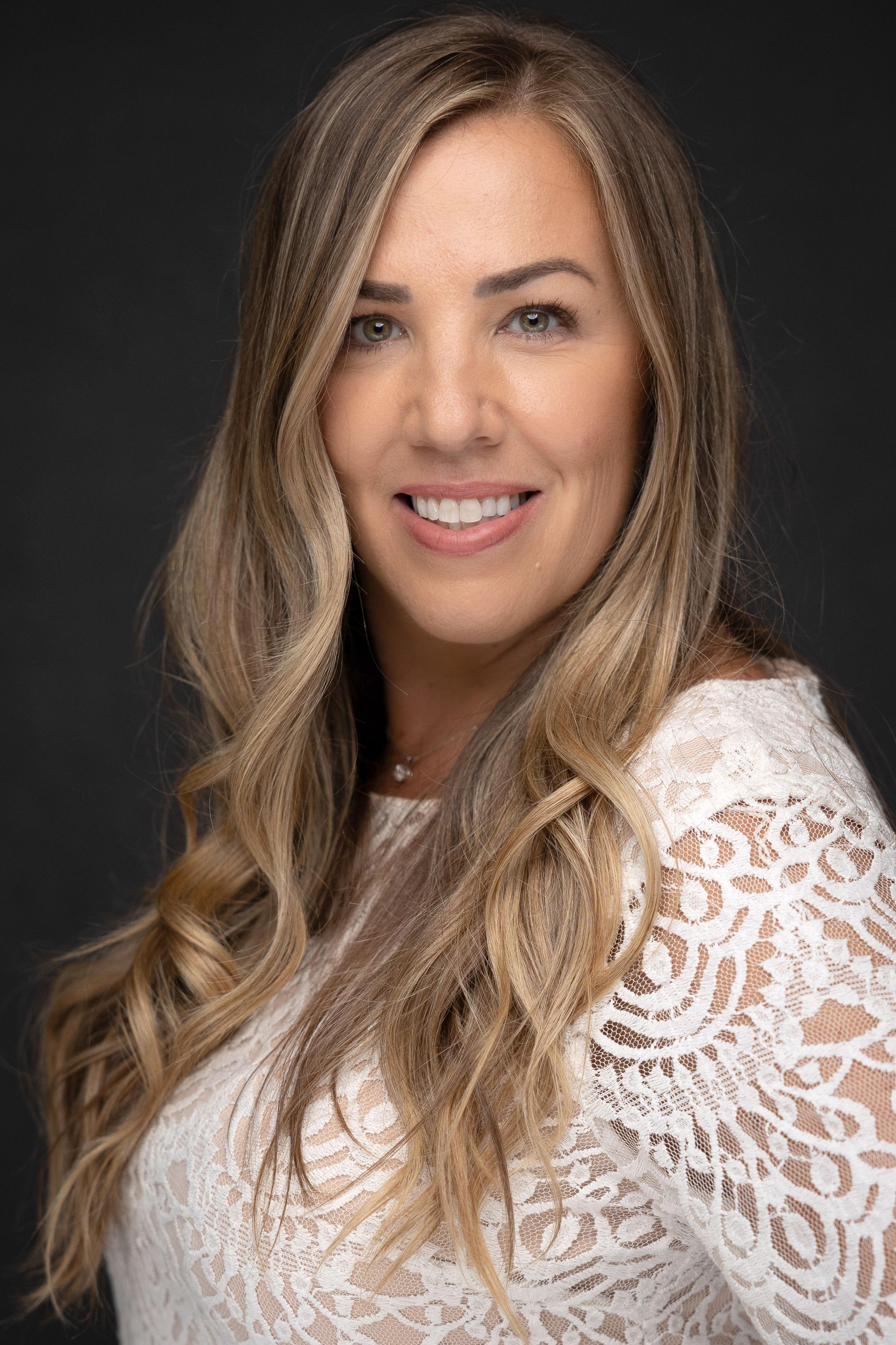 Professional headshot of a woman with long wavy hair in a white lace top