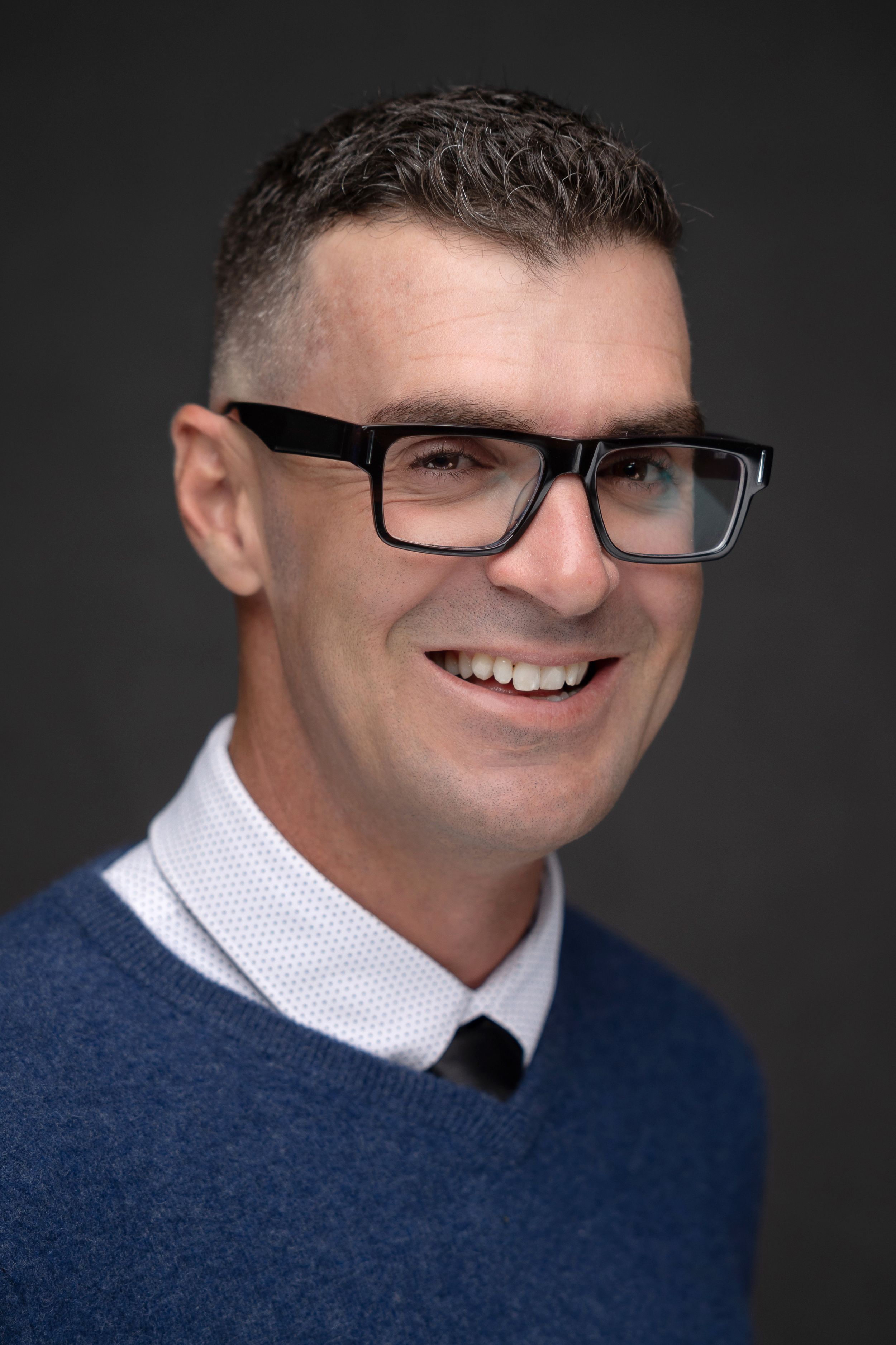 Professional headshot of a man in glasses and a navy sweater