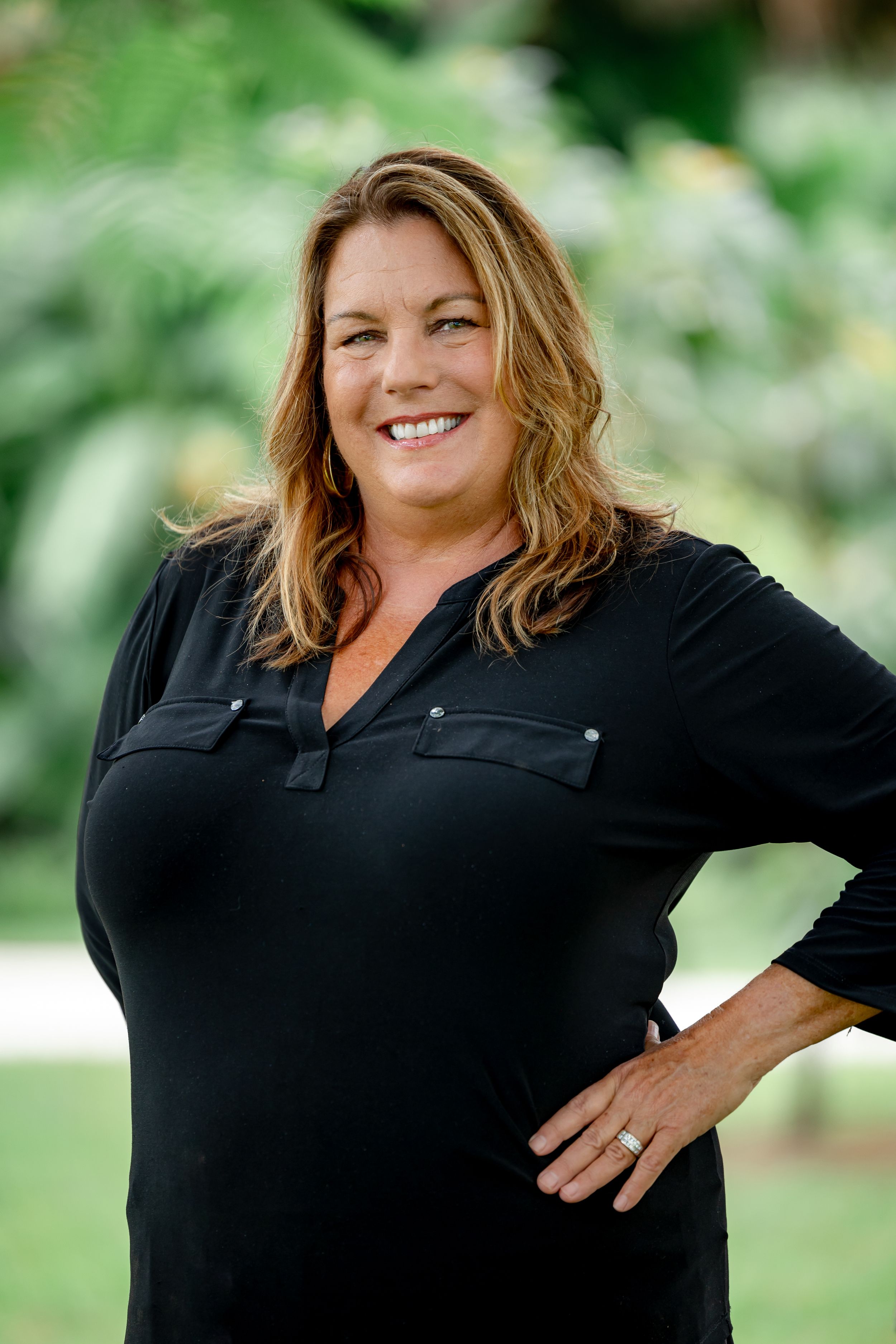 Professional headshot of a woman in a black top outdoors with greenery behind her
