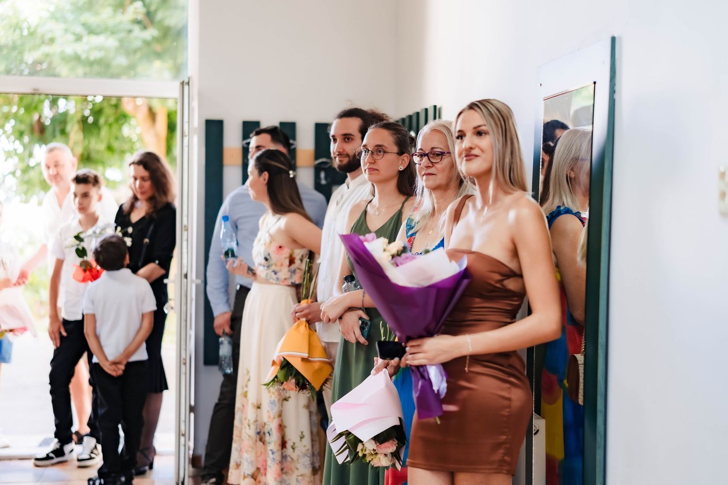Wedding guests mingle and celebrate in a bright indoor venue with natural light streaming through windows.