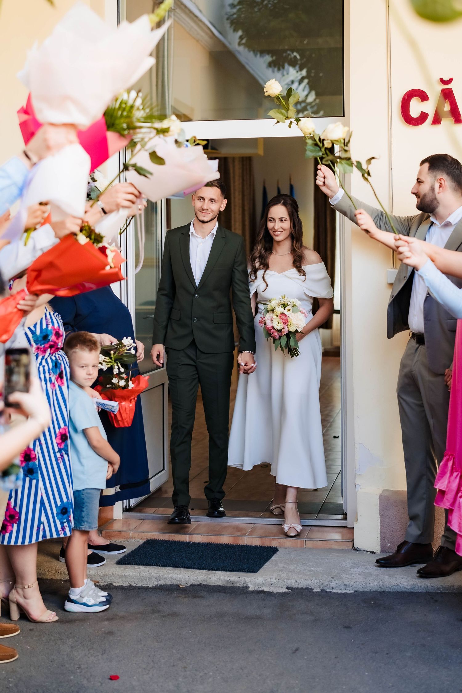 Newlyweds walk through shower of confetti and petals as guests celebrate outside venue entrance.