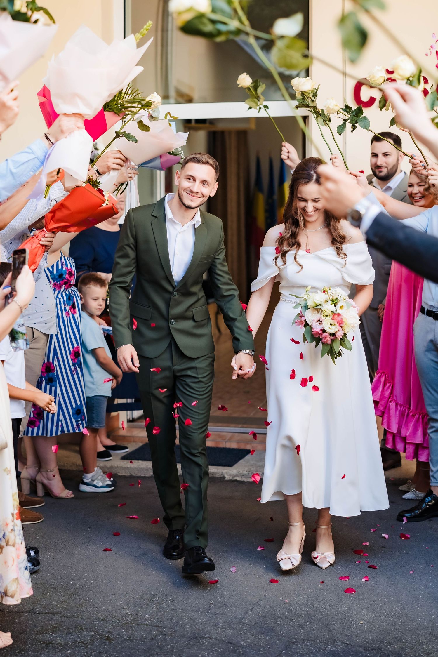 Wedding party exits venue while guests throw rose petals in celebration on outdoor steps.