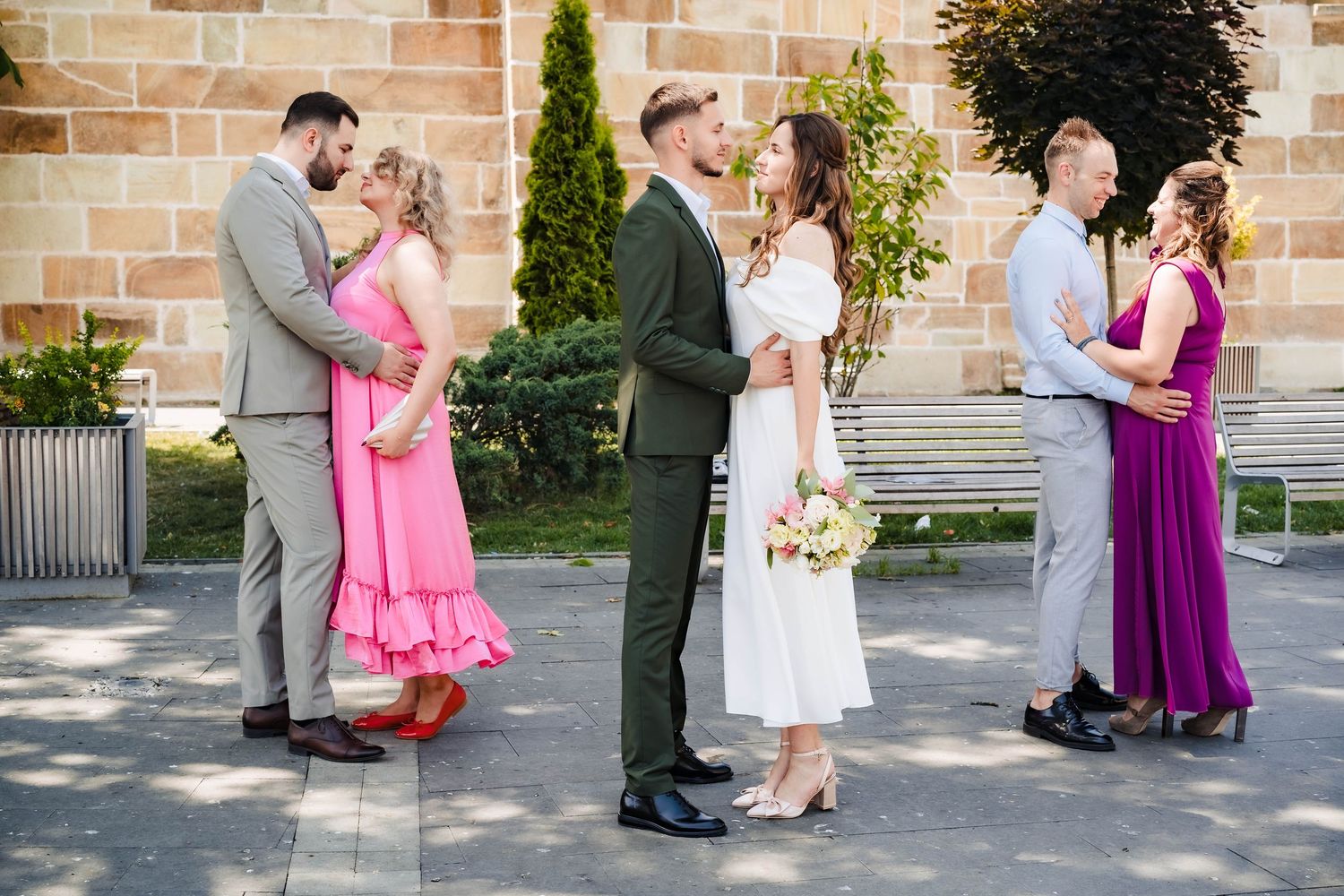 Wedding party poses together outside brick building in coordinated formal attire.
