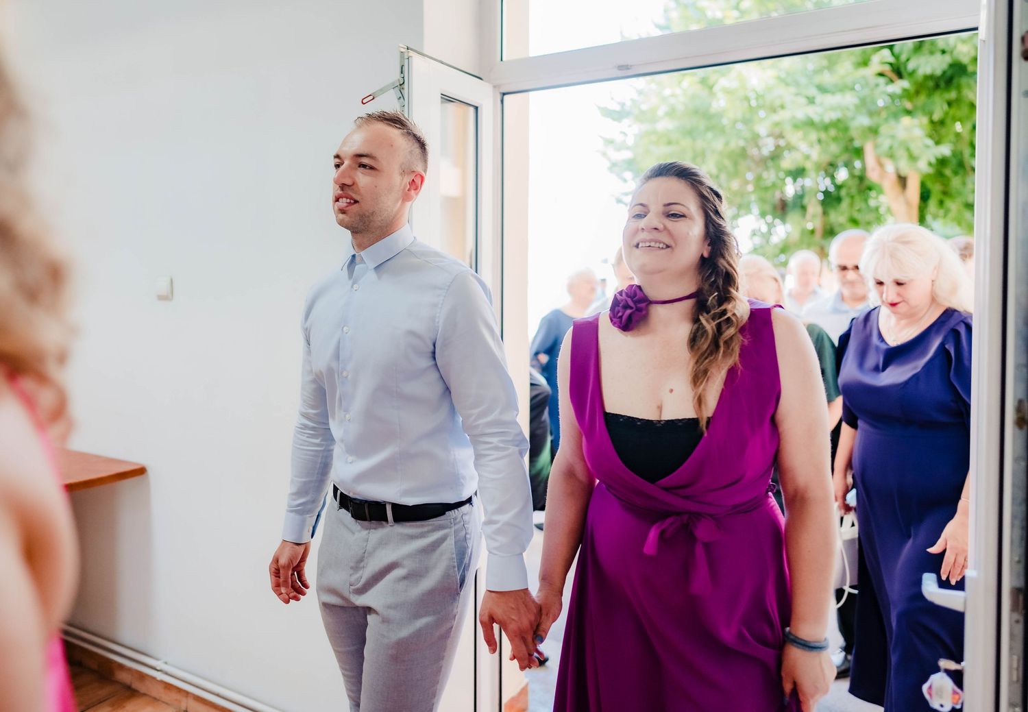 Wedding party members walking in coordinated purple and gray attire in bright indoor space.