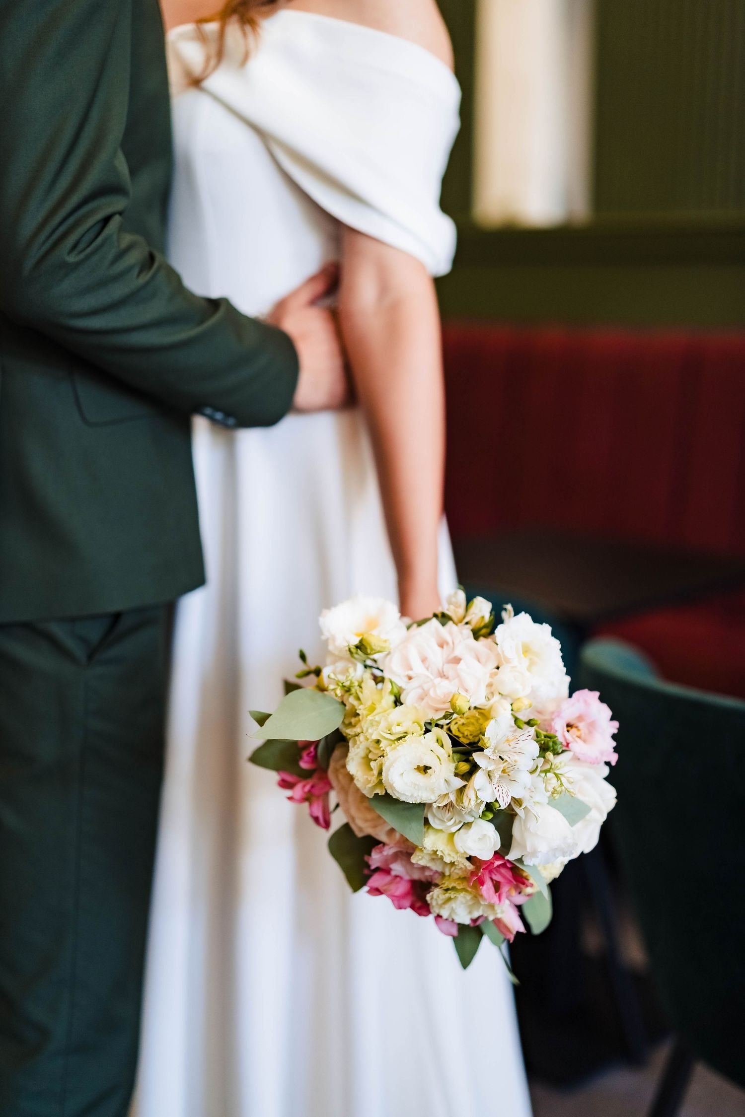 Bride in white dress holding delicate pink and yellow floral bouquet.