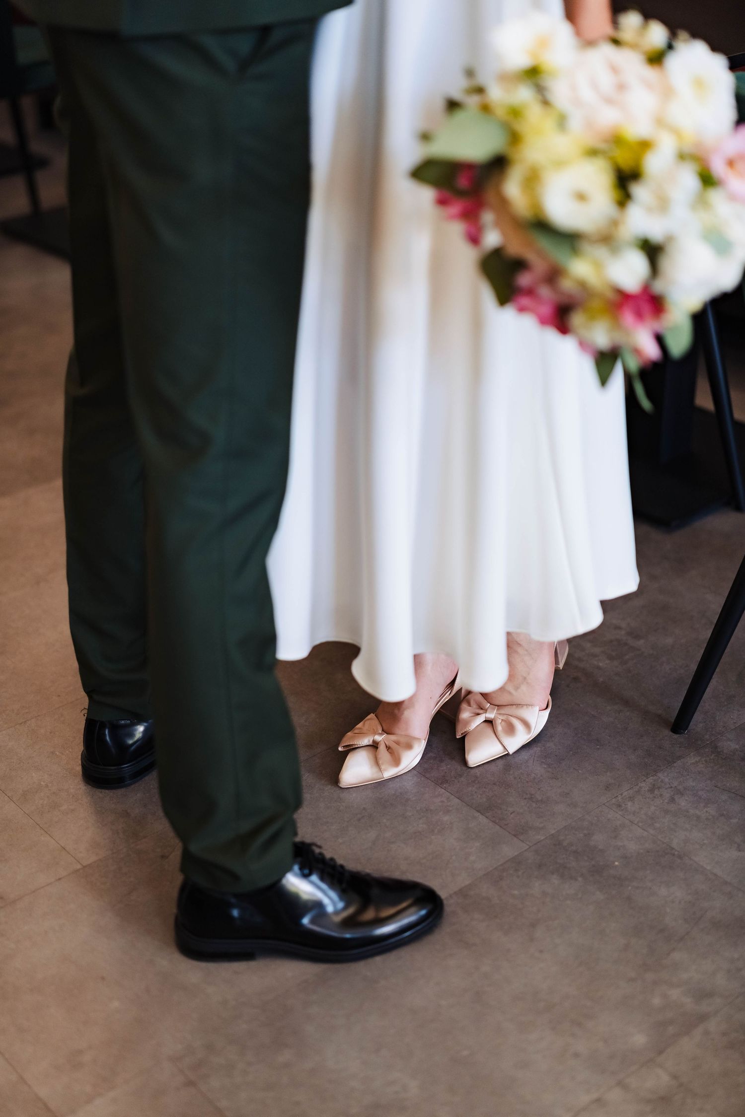 Detail shot of formal shoes and white dress hem with floral bouquet on floor.
