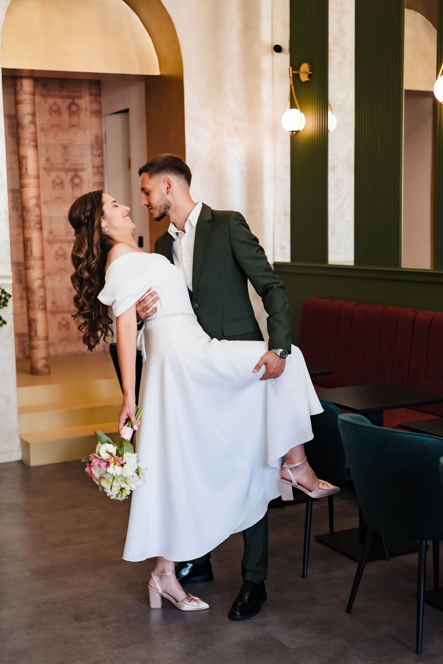 Romantic poses in elegant venue with white dress and dark suit against brick walls.