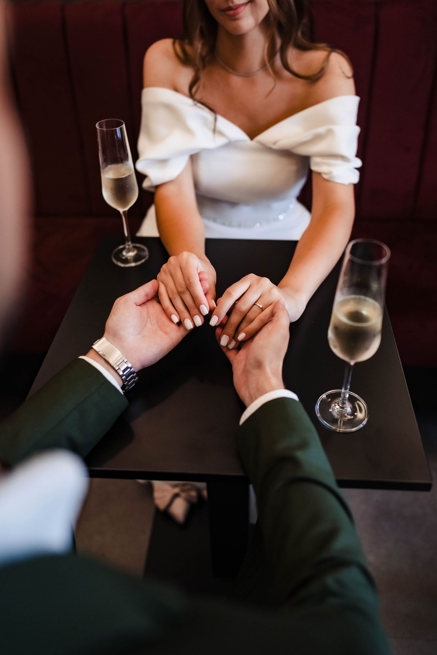Hands intertwined on dark table with champagne glasses in intimate setting.