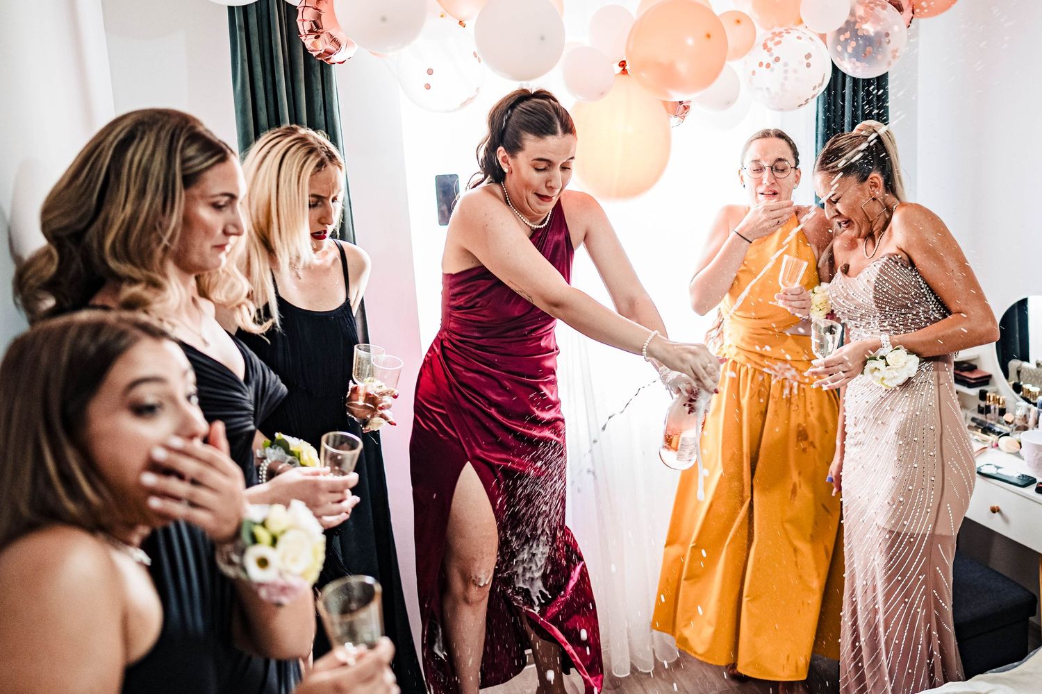 Wedding party guests in colorful dresses celebrate together in a bright indoor space.