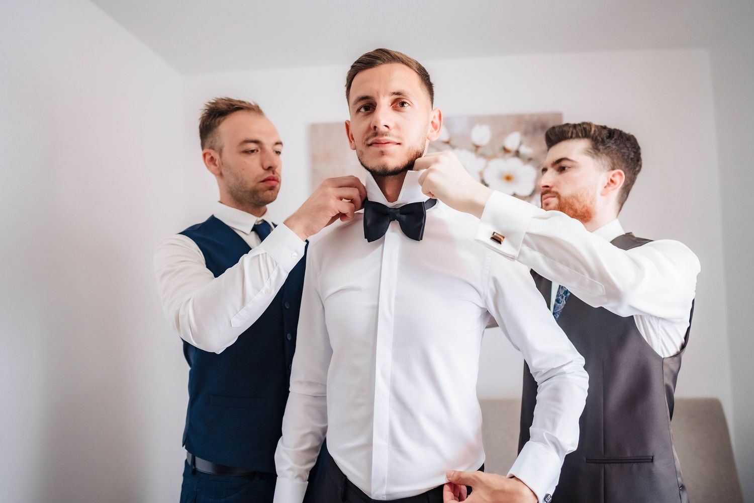 Groomsmen help adjust formal attire while getting ready for wedding ceremony.